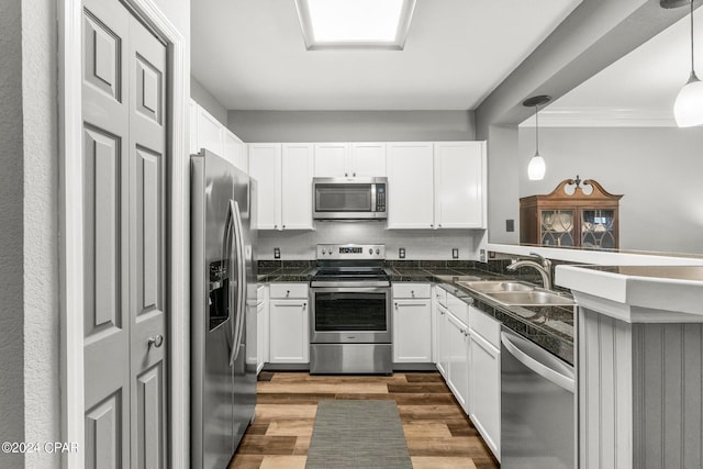 kitchen with appliances with stainless steel finishes, sink, wood-type flooring, decorative light fixtures, and white cabinets