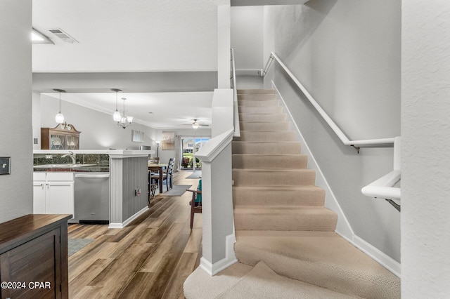 stairway featuring wood-type flooring, ceiling fan with notable chandelier, crown molding, and sink