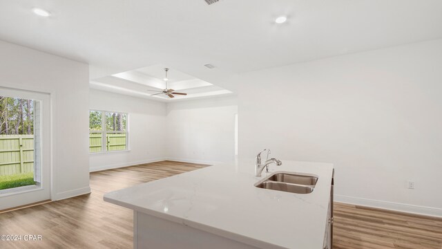 empty room with light wood-type flooring, ceiling fan, and a raised ceiling