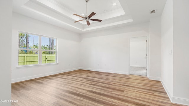 empty room featuring light hardwood / wood-style floors, ornamental molding, ceiling fan, and a tray ceiling