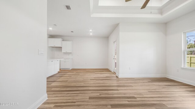 unfurnished living room featuring ceiling fan, light wood-type flooring, and a tray ceiling