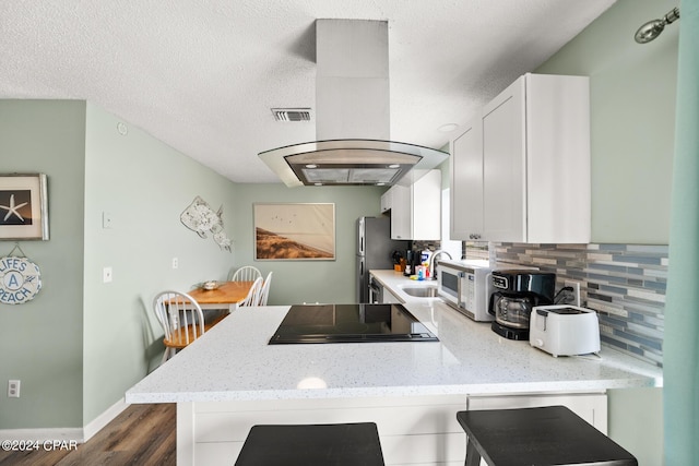 kitchen featuring tasteful backsplash, a textured ceiling, stainless steel fridge, island exhaust hood, and white cabinets