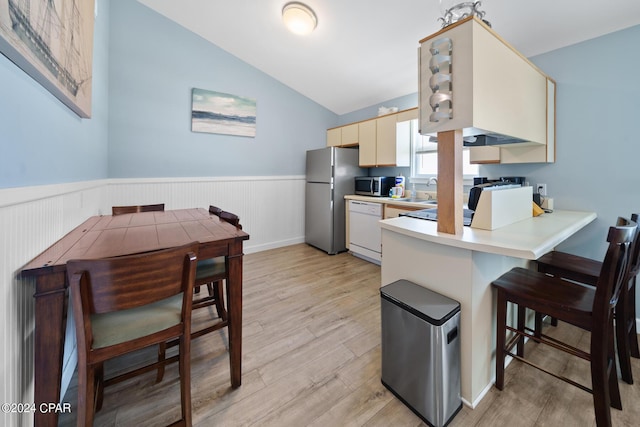 kitchen with lofted ceiling, stainless steel appliances, light hardwood / wood-style floors, kitchen peninsula, and cream cabinetry