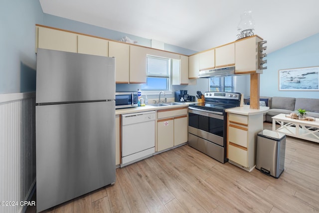 kitchen with vaulted ceiling, appliances with stainless steel finishes, sink, cream cabinetry, and light hardwood / wood-style flooring