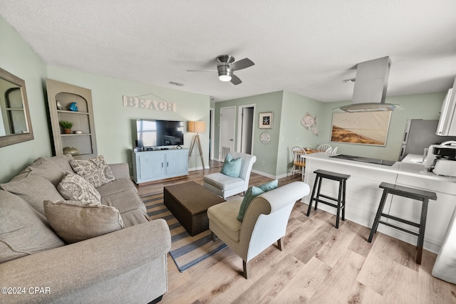 living room with light hardwood / wood-style flooring, a textured ceiling, and ceiling fan