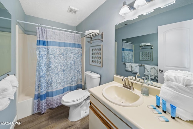 full bathroom with hardwood / wood-style floors, vanity, shower / tub combo, toilet, and a textured ceiling