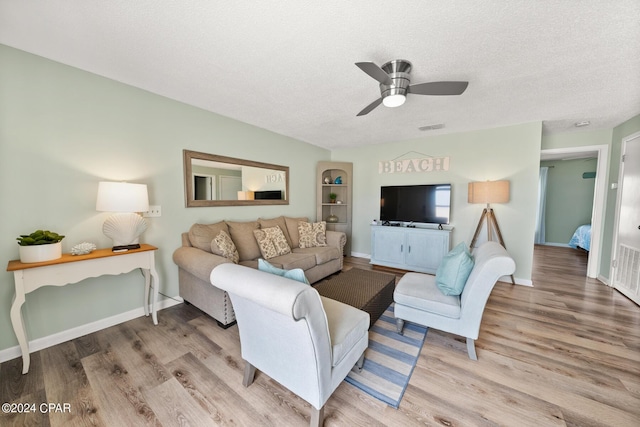 living room featuring ceiling fan, light hardwood / wood-style flooring, and a textured ceiling