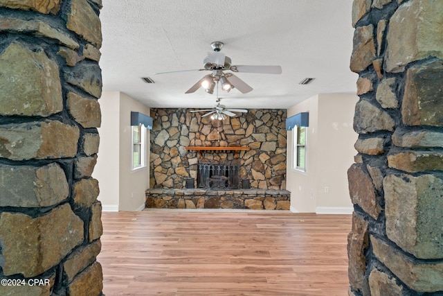 living room with ceiling fan, a stone fireplace, light wood-type flooring, and a textured ceiling