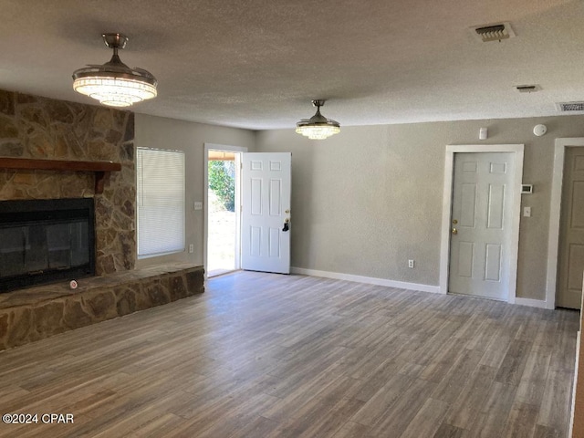 unfurnished living room with hardwood / wood-style flooring, a stone fireplace, and a textured ceiling