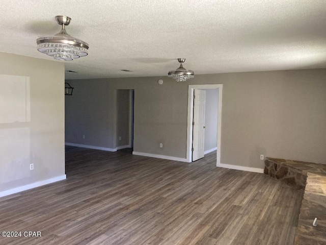 empty room featuring a textured ceiling, dark hardwood / wood-style floors, and an inviting chandelier