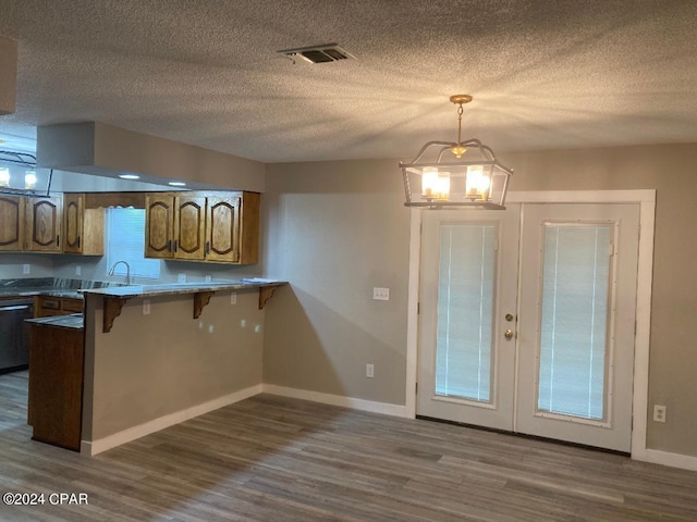 kitchen featuring hanging light fixtures, dark hardwood / wood-style flooring, a notable chandelier, kitchen peninsula, and a kitchen bar