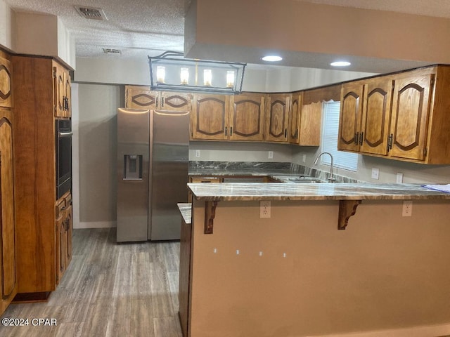 kitchen with kitchen peninsula, sink, stainless steel fridge with ice dispenser, oven, and a breakfast bar area