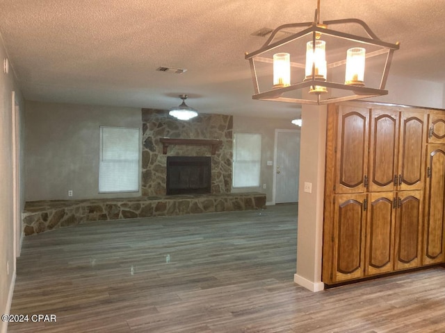 unfurnished living room featuring hardwood / wood-style flooring, a stone fireplace, a textured ceiling, and an inviting chandelier