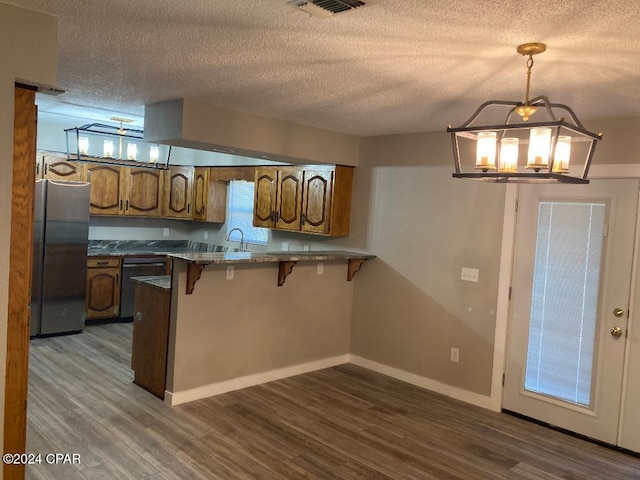 kitchen featuring stainless steel refrigerator, kitchen peninsula, hanging light fixtures, and dark wood-type flooring