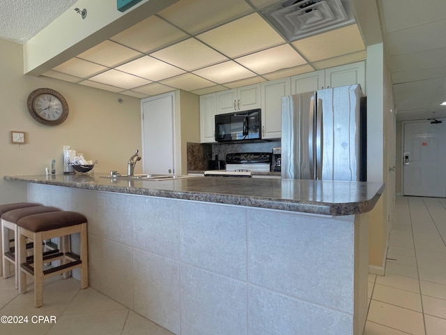 kitchen featuring black appliances, kitchen peninsula, light tile patterned floors, and sink