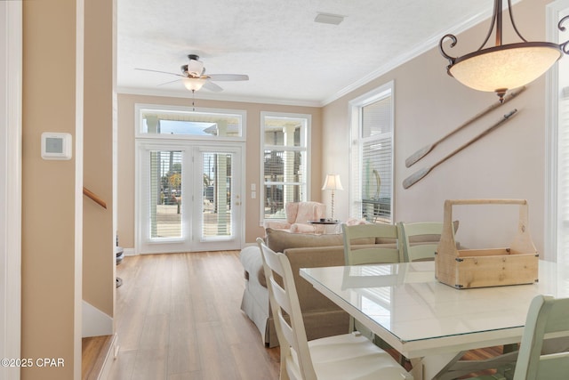 dining area with ceiling fan, ornamental molding, a textured ceiling, and light wood-type flooring