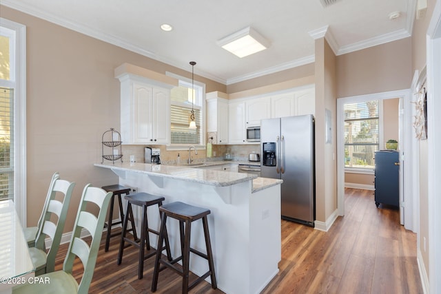 kitchen featuring appliances with stainless steel finishes, white cabinets, hanging light fixtures, light stone counters, and kitchen peninsula