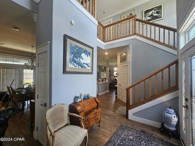 entryway with ornamental molding, a notable chandelier, a towering ceiling, and dark wood-type flooring