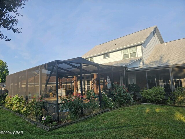 rear view of house with glass enclosure, a patio area, and a lawn