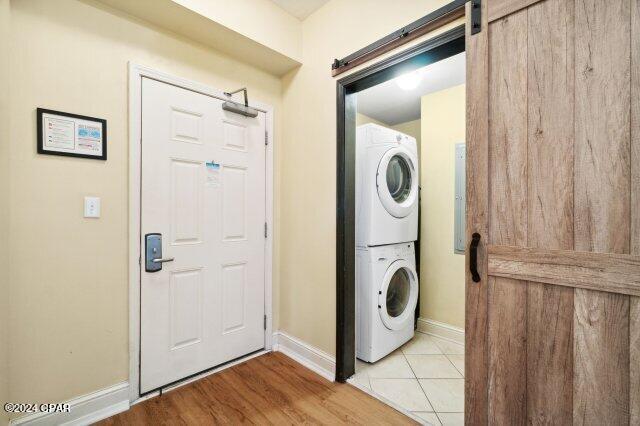 laundry room with stacked washer and dryer, light hardwood / wood-style flooring, and a barn door