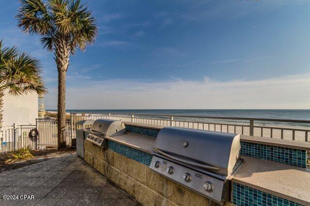 view of patio / terrace with a water view, grilling area, a beach view, and exterior kitchen