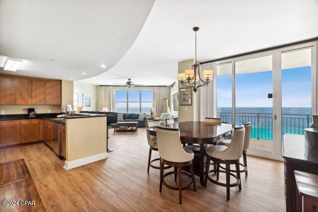 dining room featuring expansive windows, a water view, ceiling fan with notable chandelier, and light wood-type flooring