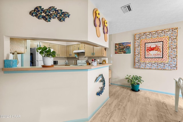 kitchen with a textured ceiling, under cabinet range hood, white appliances, visible vents, and light countertops