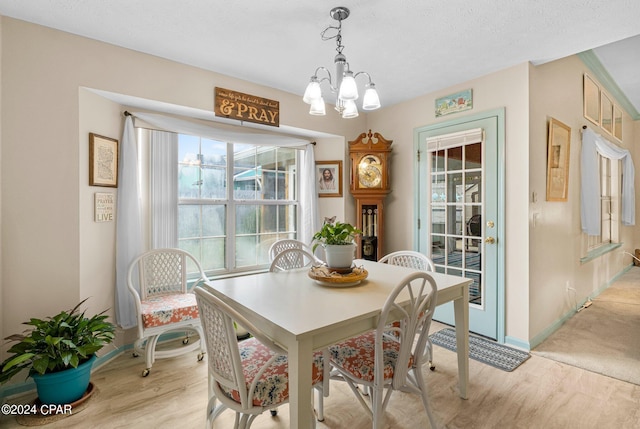 dining space featuring light wood-style floors, a textured ceiling, baseboards, and a notable chandelier