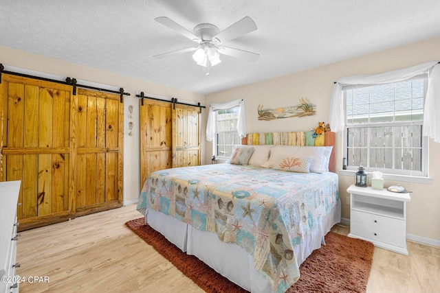 bedroom featuring a textured ceiling, a barn door, light wood-style flooring, and baseboards