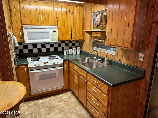 kitchen featuring light tile patterned flooring, decorative backsplash, white appliances, sink, and wood walls