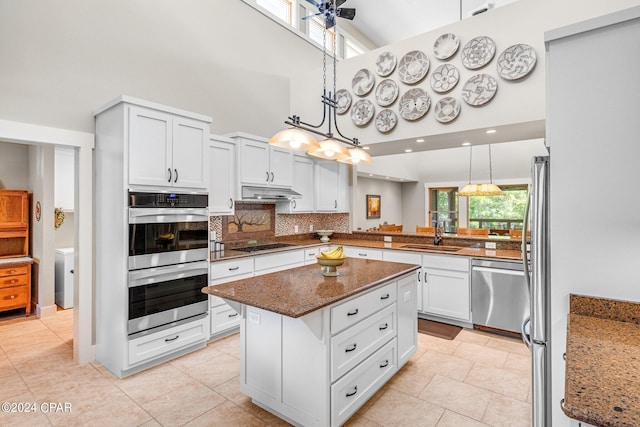 kitchen featuring stainless steel appliances, dark stone counters, a center island, ceiling fan, and a towering ceiling