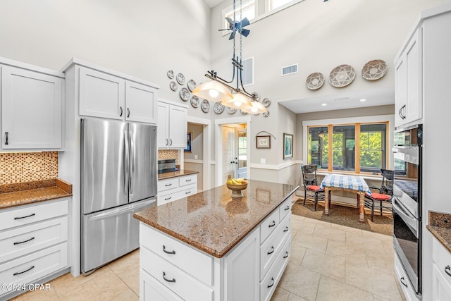 kitchen featuring backsplash, a high ceiling, white cabinets, light tile patterned floors, and stainless steel appliances