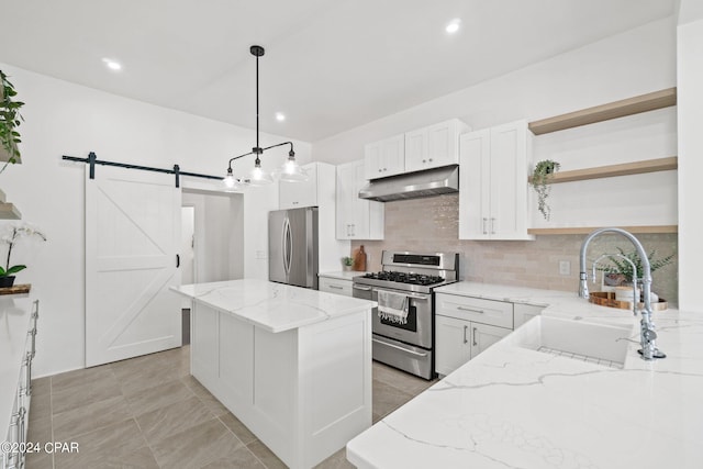 kitchen featuring light tile patterned flooring, a barn door, light stone countertops, appliances with stainless steel finishes, and decorative light fixtures