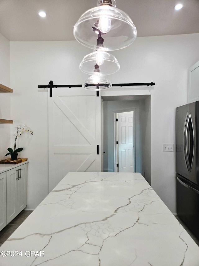 interior space with white cabinetry, hanging light fixtures, black fridge, and a barn door