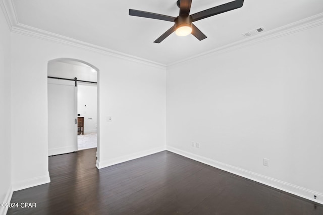 empty room featuring dark wood-type flooring, ornamental molding, ceiling fan, and a barn door