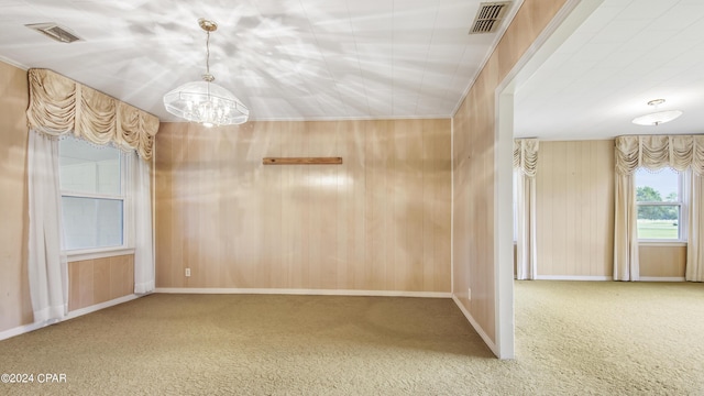 empty room featuring carpet floors, crown molding, a notable chandelier, and wood walls