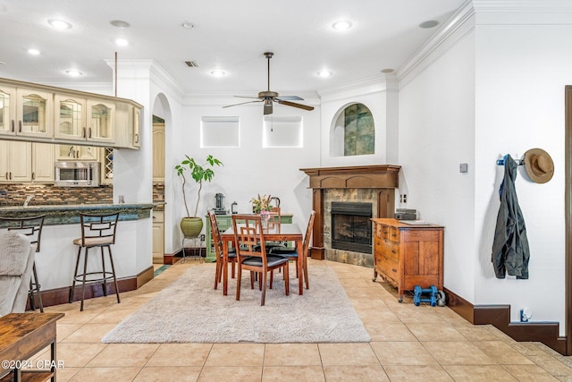 dining area with a tiled fireplace, ceiling fan, crown molding, and light tile patterned floors