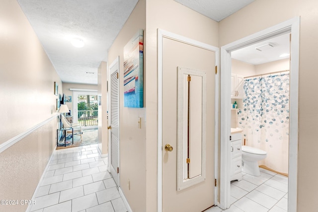 hallway with a textured ceiling and light tile patterned flooring