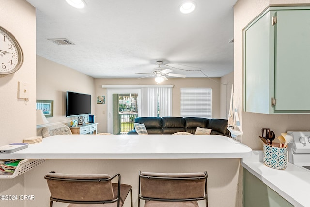 kitchen featuring kitchen peninsula, green cabinets, ceiling fan, and a kitchen bar