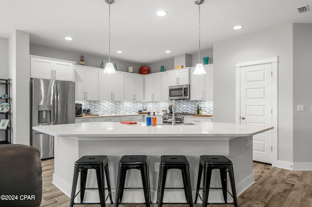 kitchen featuring a breakfast bar area, white cabinetry, a center island with sink, and stainless steel appliances