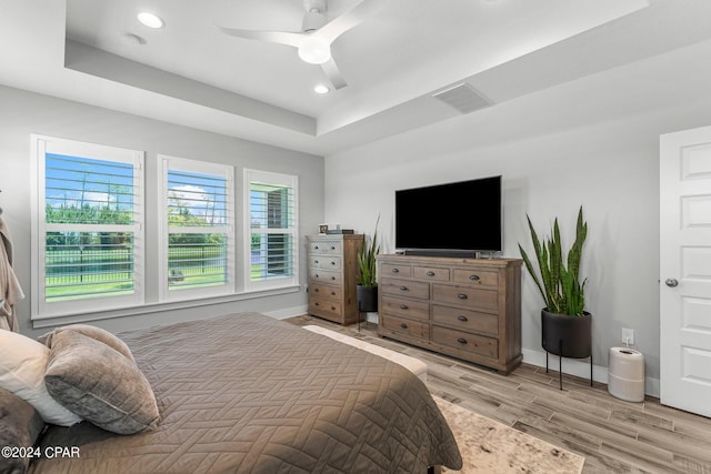 bedroom with ceiling fan, light hardwood / wood-style floors, and a tray ceiling