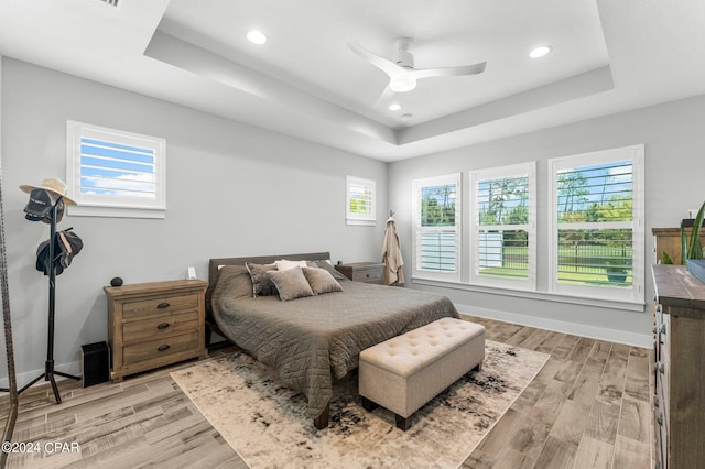 bedroom featuring multiple windows, a tray ceiling, ceiling fan, and light hardwood / wood-style floors