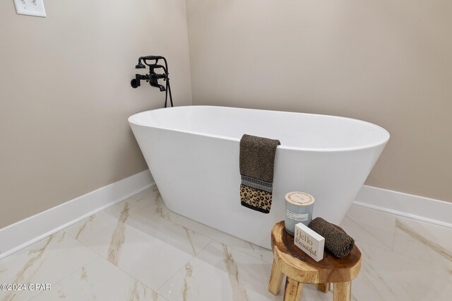 full bath with marble finish floor, a soaking tub, and baseboards