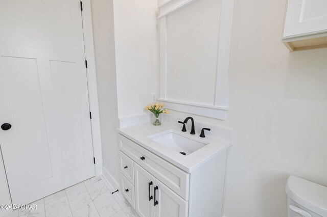 half bathroom featuring marble finish floor, vanity, and toilet