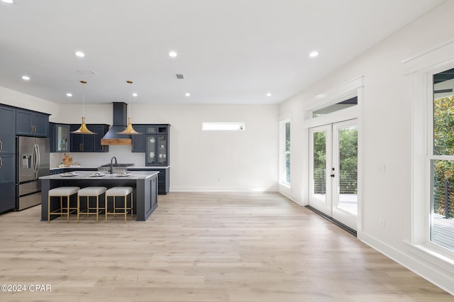 kitchen with a kitchen bar, french doors, a kitchen island with sink, stainless steel fridge with ice dispenser, and hanging light fixtures