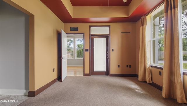 foyer entrance featuring a tray ceiling and light carpet