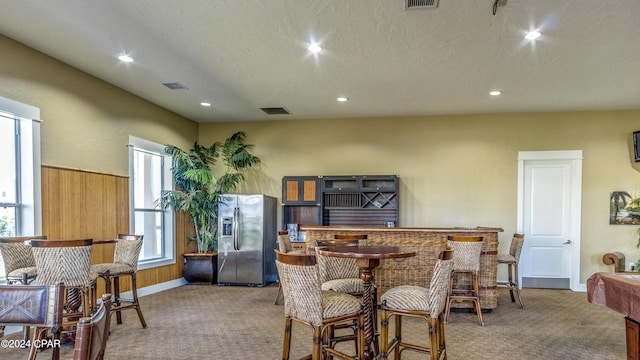 dining area featuring light colored carpet, a textured ceiling, and wooden walls