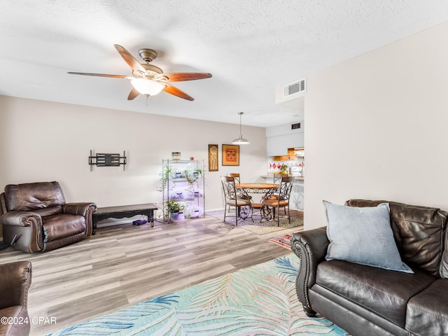 living room with ceiling fan, a textured ceiling, and light hardwood / wood-style floors