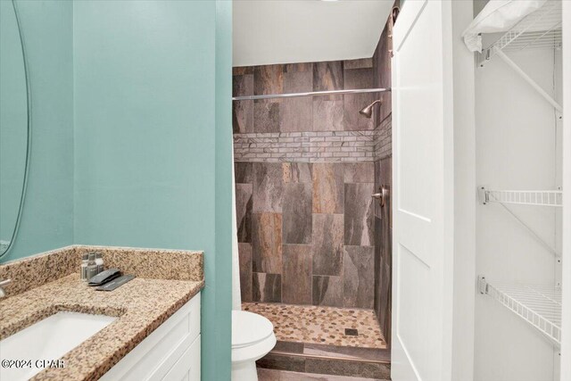 bathroom with toilet, a tile shower, and vanity