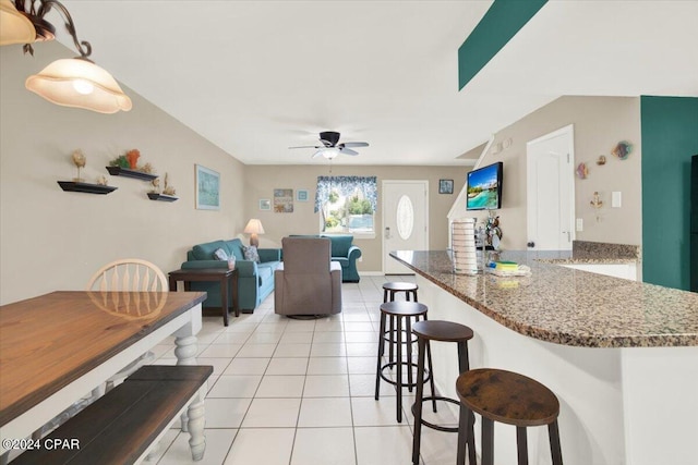 kitchen featuring ceiling fan, a breakfast bar, stone countertops, light tile patterned floors, and kitchen peninsula